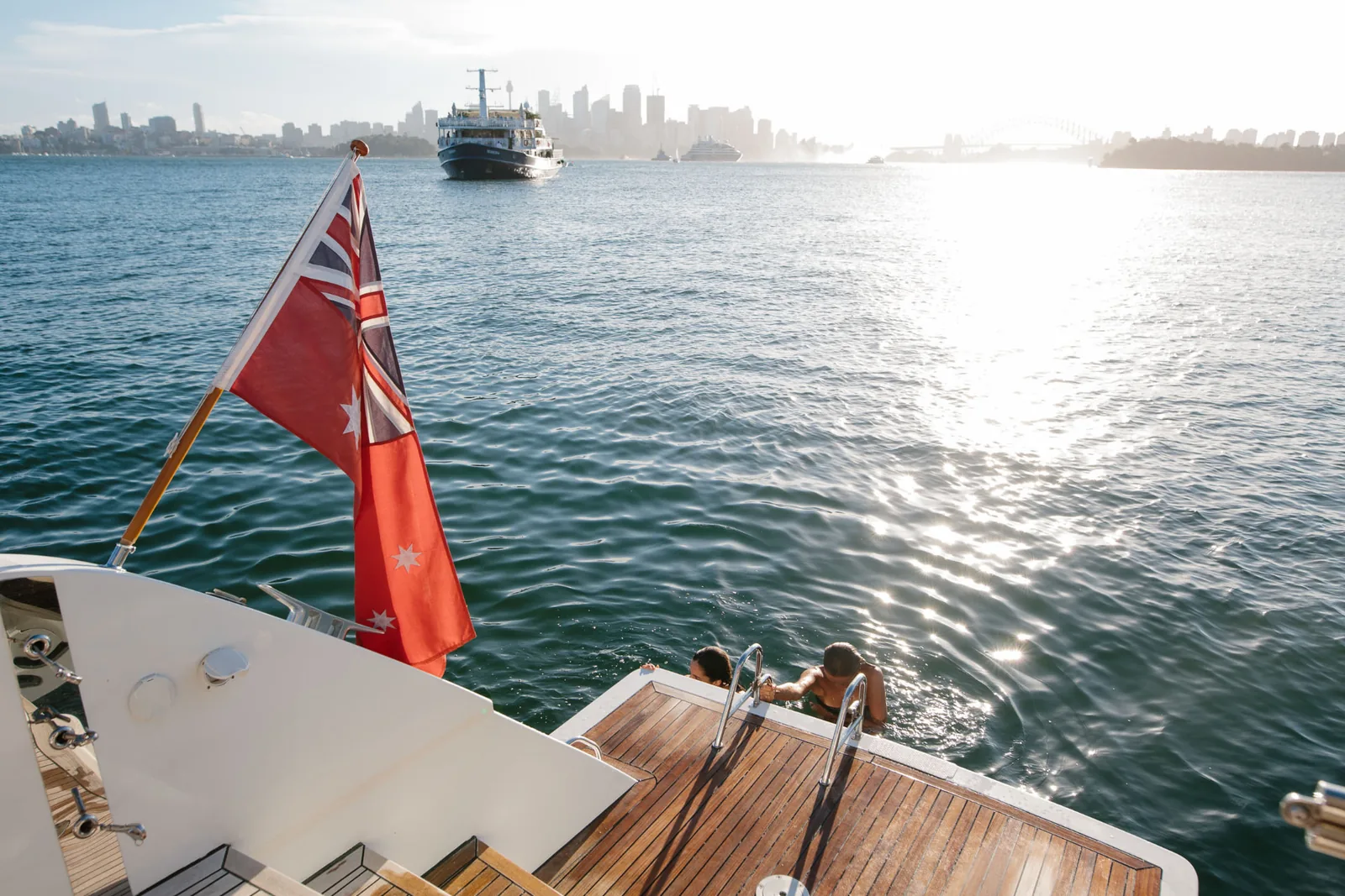 Guests swimming from Mon Rêve's aft platform with the Sydney skyline beyond