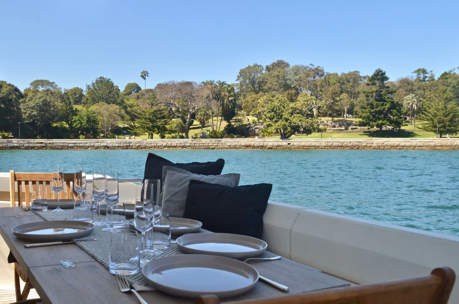 The Ribbon aft deck dining table set with glassware, looking across the harbour to the Royal Botanic Garden