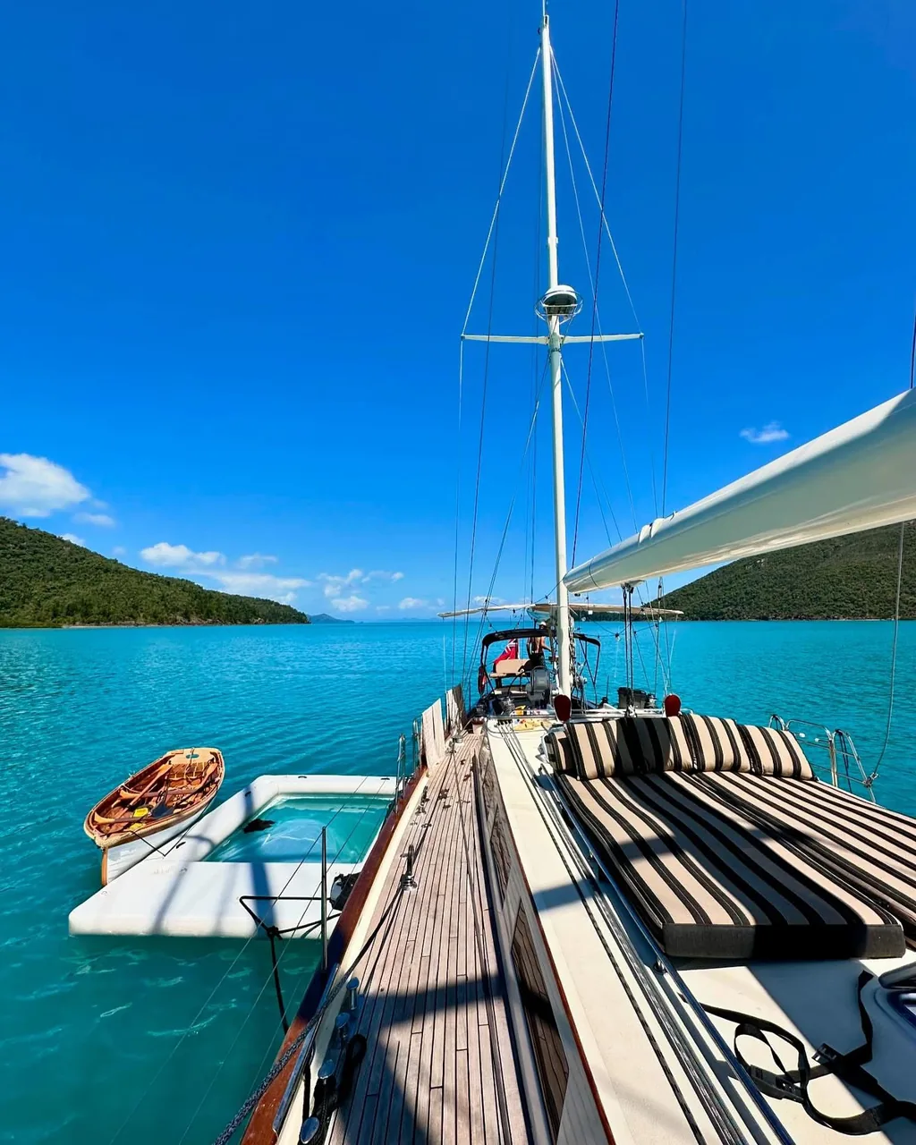 Sir Thomas Sopwith's teak side deck and striped sunbathing cushions beside a floating swim platform in turquoise water
