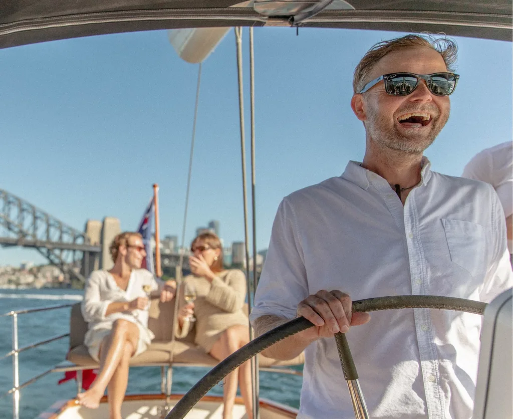 Jeremy at the helm on Sydney Harbour with guests aboard and the Harbour Bridge behind