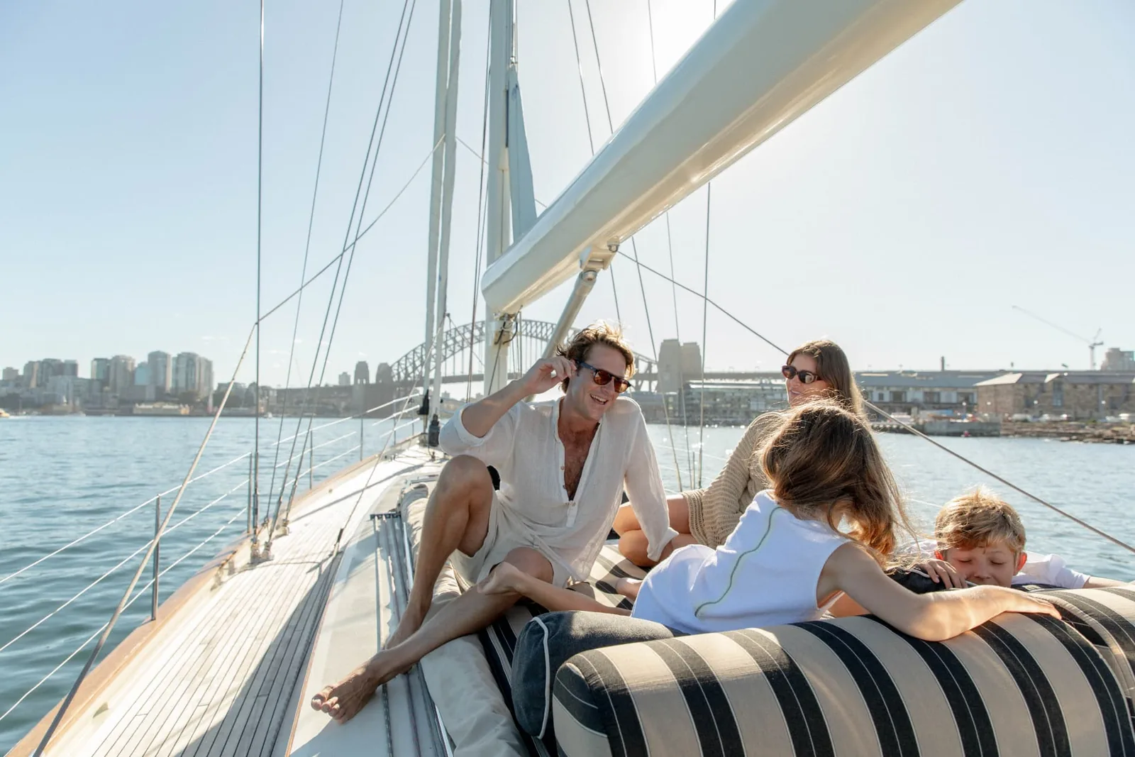 Guests relaxing on the foredeck of a sailing yacht with the Sydney Harbour Bridge behind