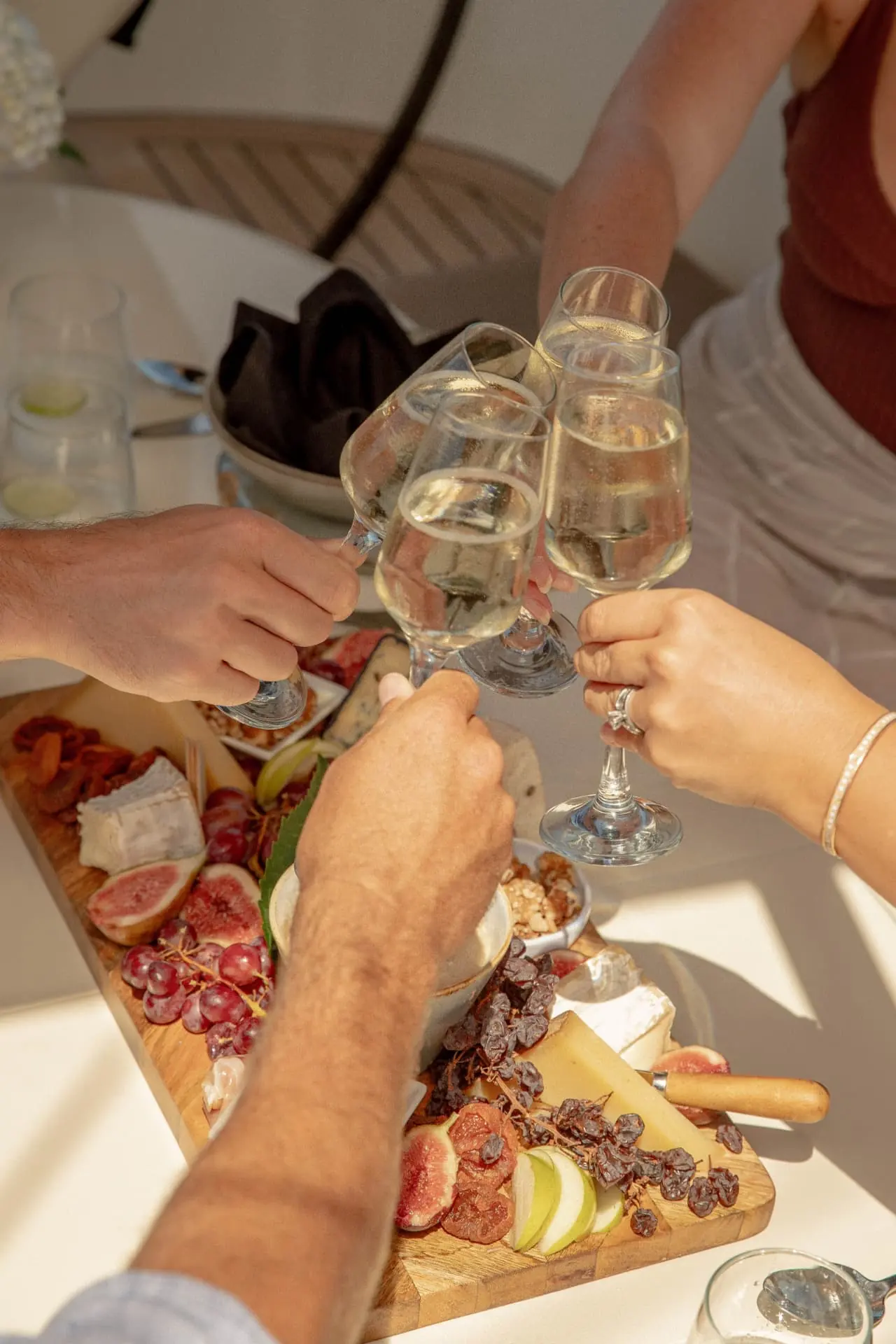 Guests toasting with glasses of sparkling wine over a grazing board on the deck of a charter yacht