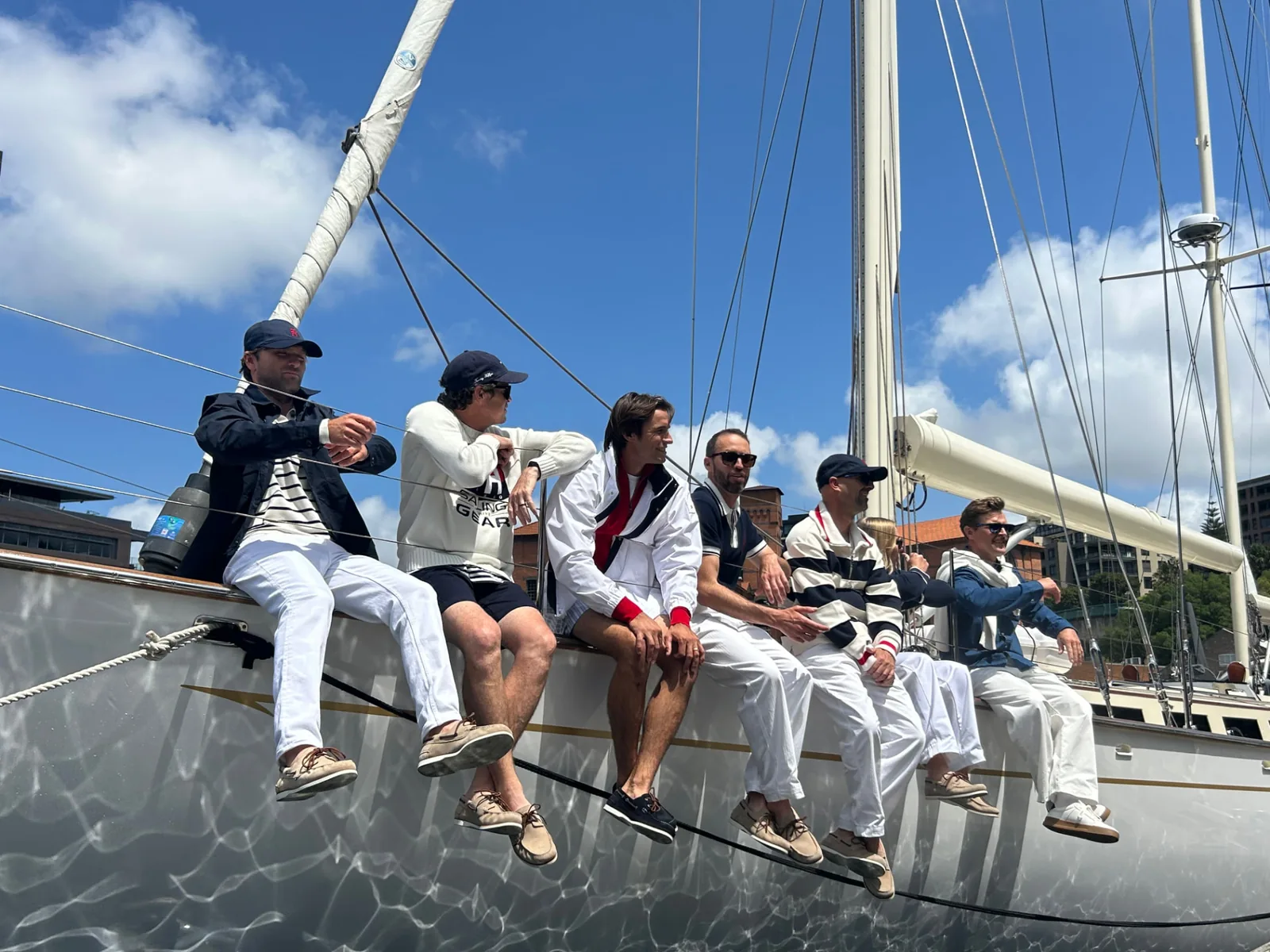 A group of guests sitting along the rail of the classic sailing yacht Sir Thomas Sopwith on Sydney Harbour