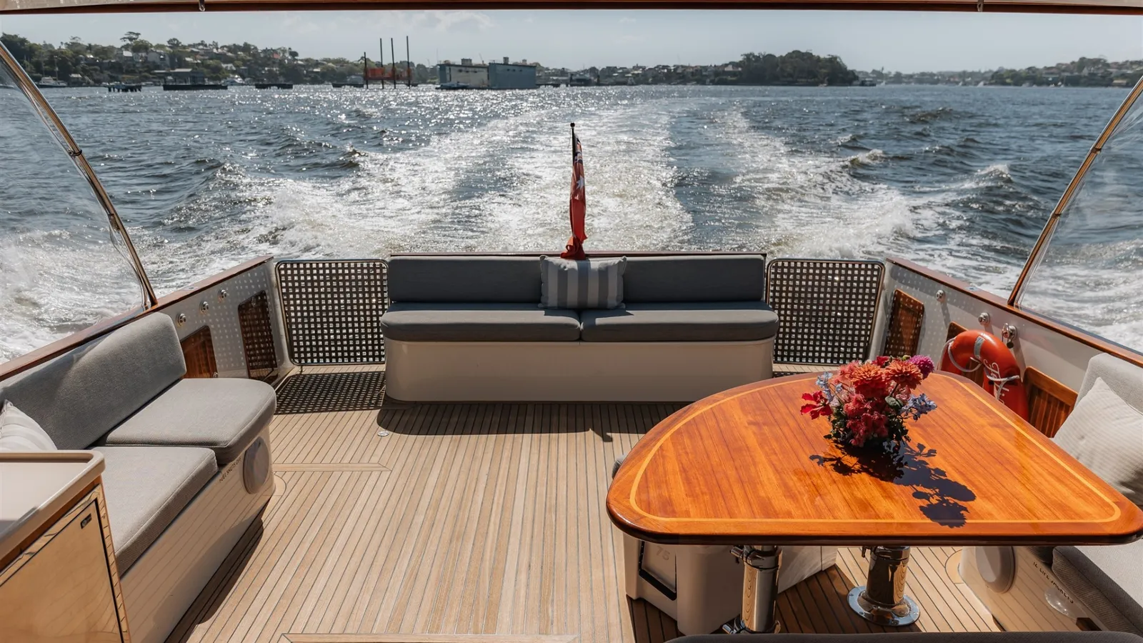 Felix's teak aft deck with lounge seating and a timber table set with flowers, cruising on the harbour