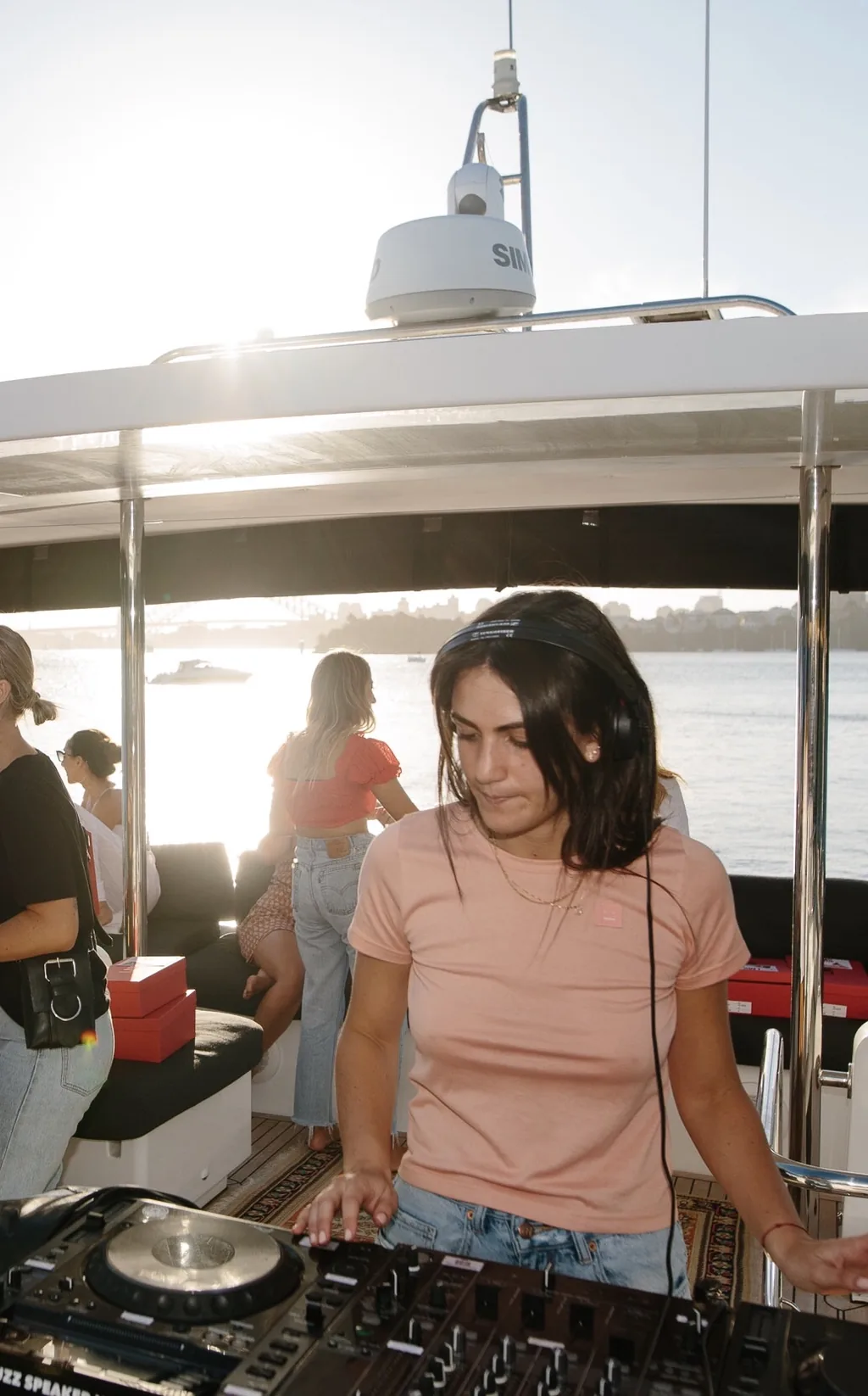 A DJ playing music on the deck of a charter yacht on Sydney Harbour at sunset